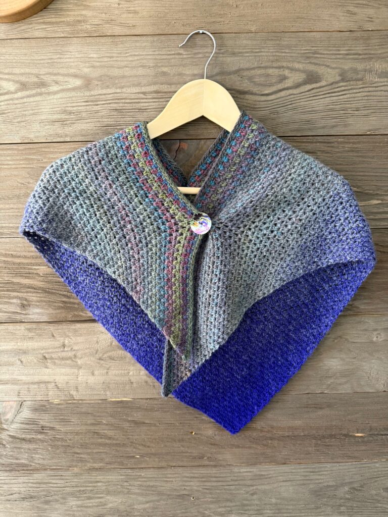 Image of a knitted multicolored striped shawl with button closure.